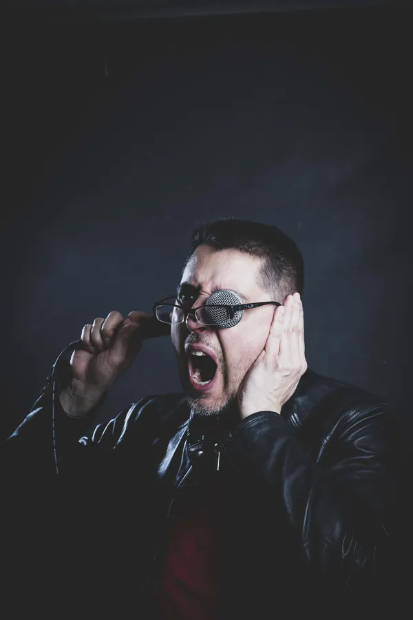 Retrato conceptual: la cabeza del micrófono apoyada sobre el ojo mientras grita.