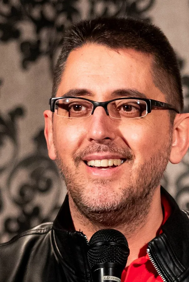 Marcos Félix sonriendo en primer plano, con gafas y chaqueta de cuero, junto al micrófono.
